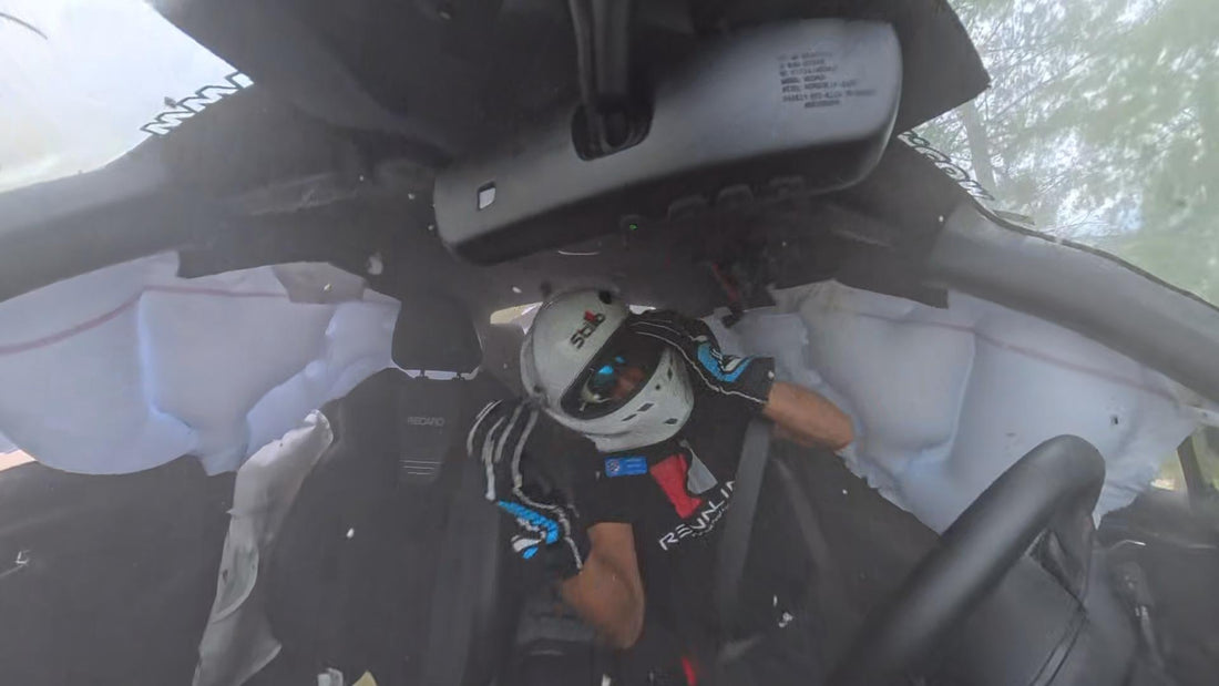 Driver hanging out of a stock seat with arms loose while the car slides upside down at Summit Point, restrained only by a three-point belt